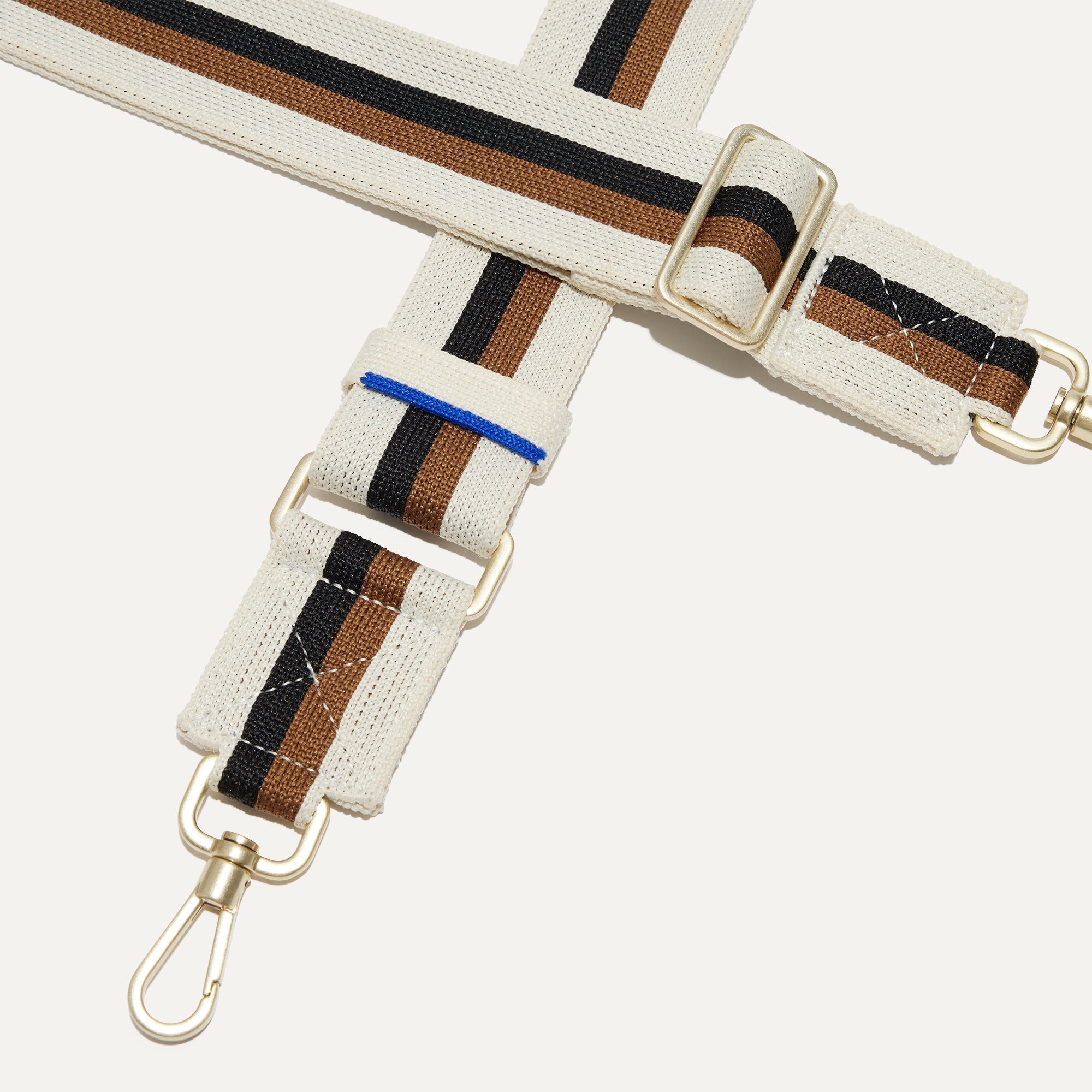 A closeup of The Crossbody Strap in White Portobello Stripe, focusing on the end snap hooks and sliding buckle.