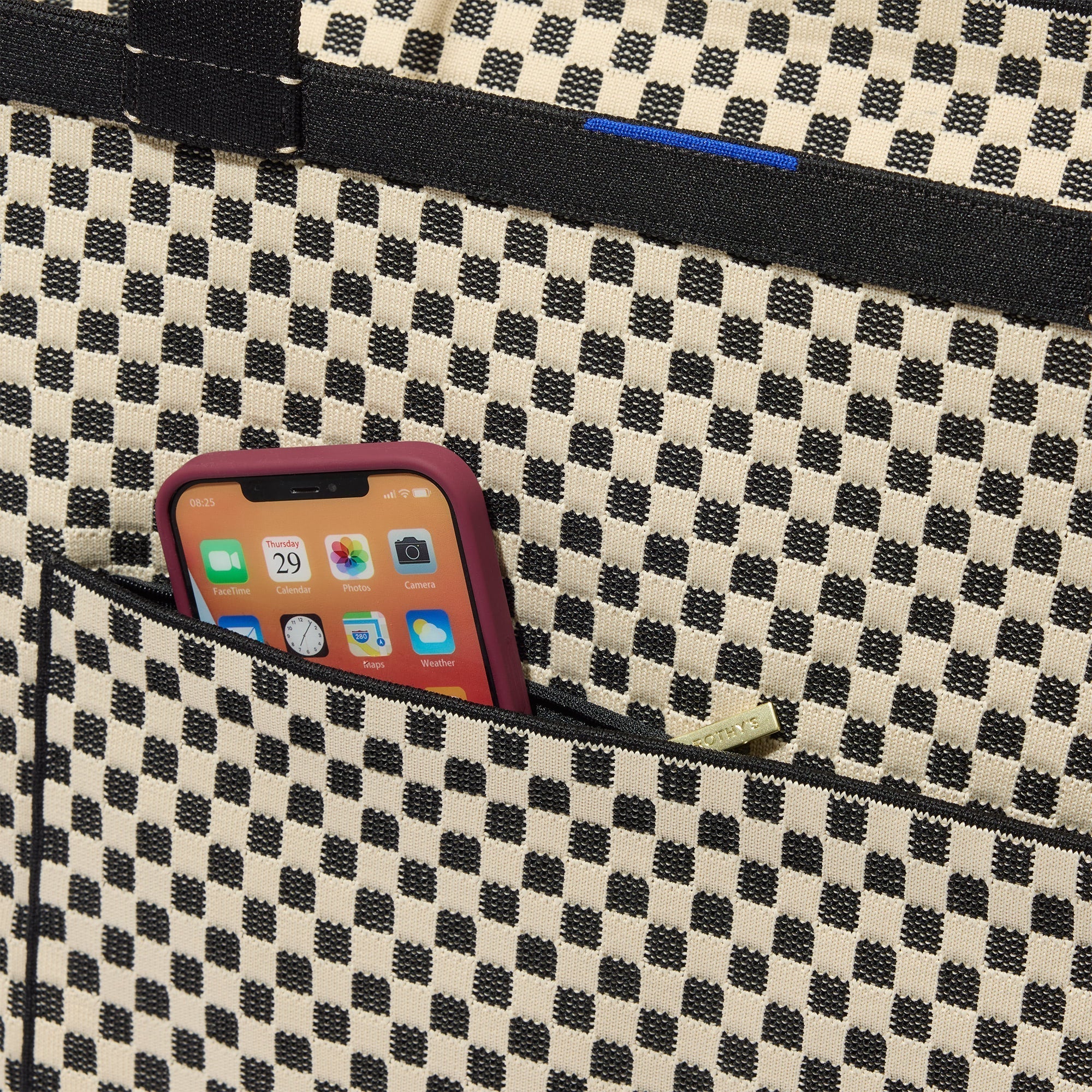 A close up of The Zip Travel Tote in Tuxedo Midi Check with a phone slipped into the outer pocket.